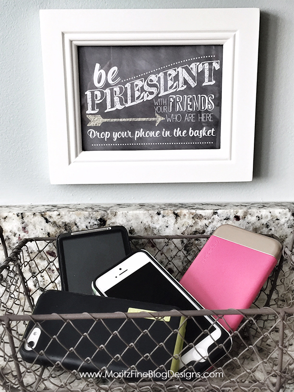 Chalkboard that says be present with friends who are here drop your phone in a basket. Basket with phones inside.