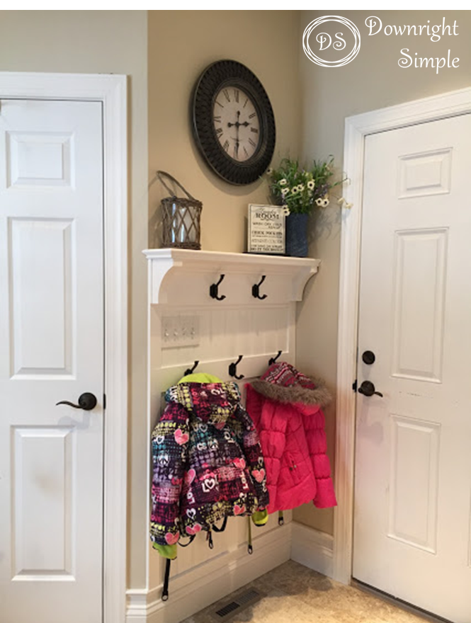 Entryway door with hooks shelf, clock. Jackets hanging on hooks.