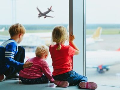 3 children watching airplanes from airport window (to represent Families Fly Free)