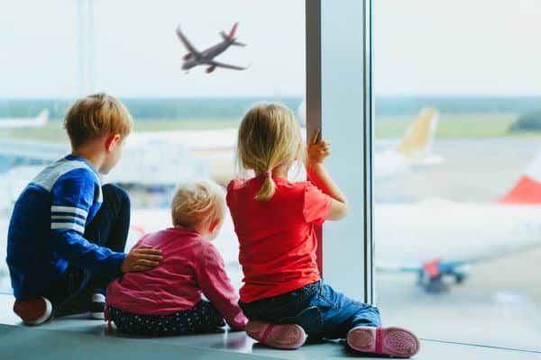 3 children watching airplanes from airport window (to represent Families Fly Free)