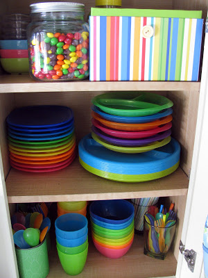 Colorful plastic cups, bowls, spoons organized in a cabinet.