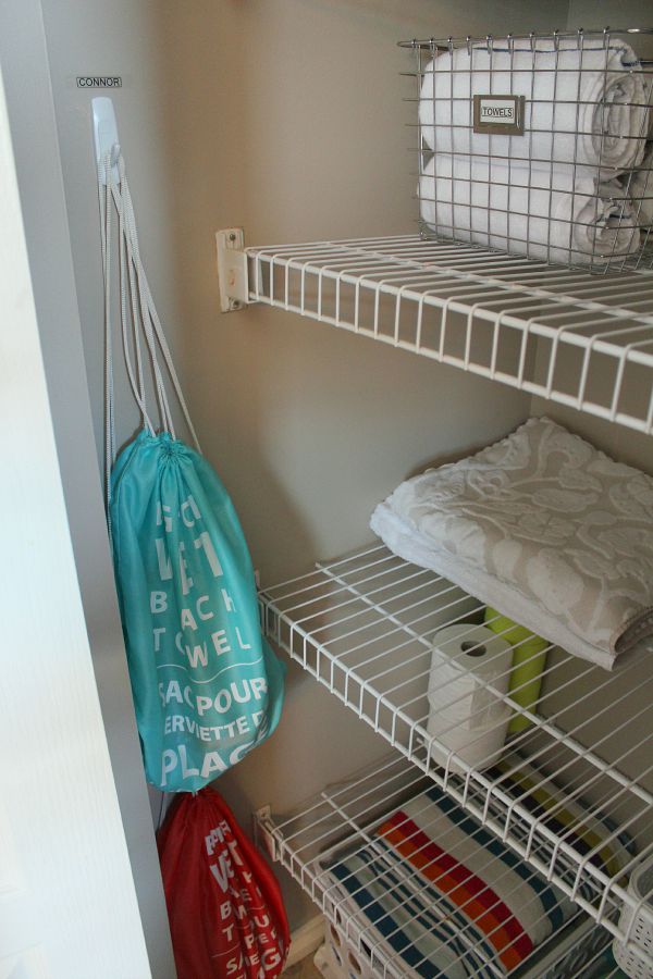 linen closet with wired shelving organized with wire basket for towels and swim bags on hooks on the wall