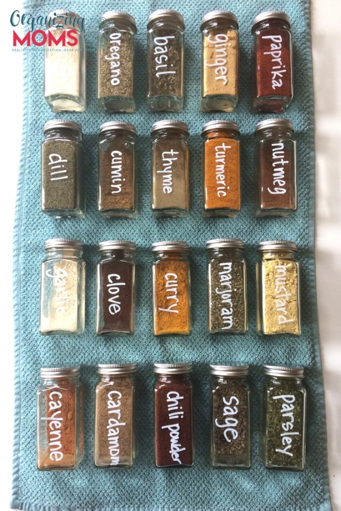 A close up filled square spice bottles labeled with white chalk marker on blue background