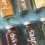 Square spice jars labeled with white markers on top of blue towel