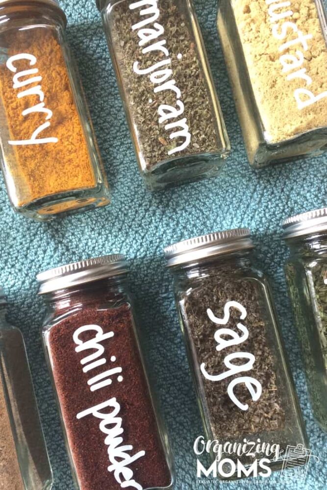 Square spice jars labeled with white markers on top of blue towel