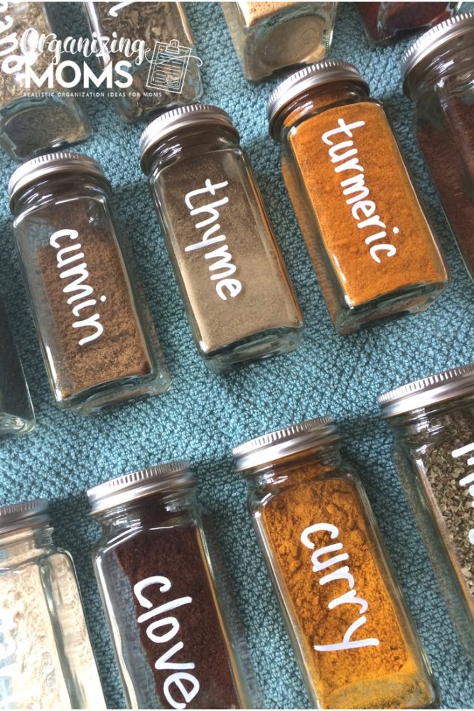 A close up filled square spice bottles labeled with white chalk marker on blue background