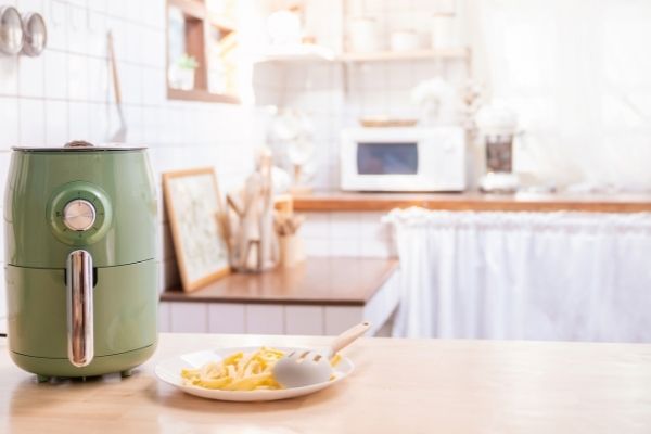 green air fryer with plate of fries in white kitchen