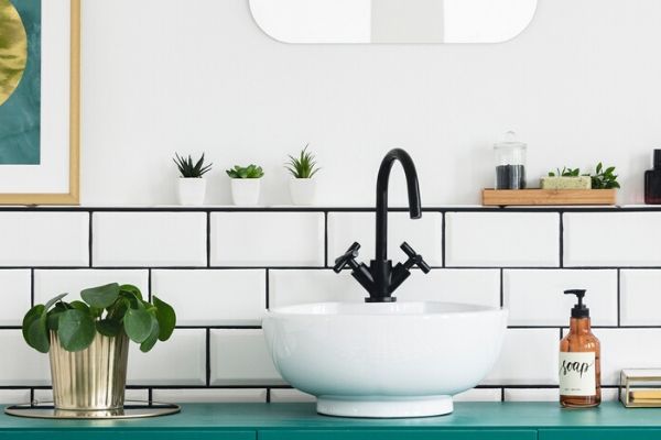 A small bathroom sink in front of white tile, plants