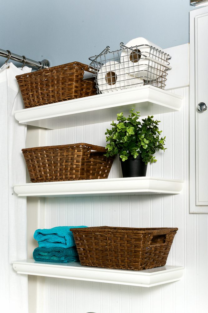 shite shelving holding wicker baskets, metal baskets storing toilet paper, blue towels and a plant