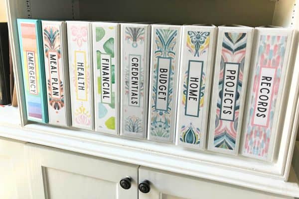 White binders with binder cover spine designs on white bookshelf.