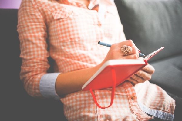 woman writing in red journal