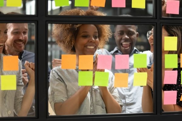 woman smiling because she achieved goal looking at colored postits on window