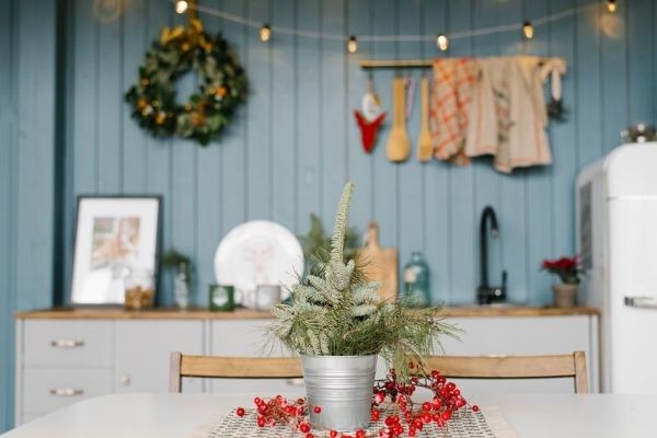 A kitchen decorated for Christmas filled with furniture and vase with evergreen cuttings on a table