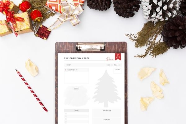 christmas tree printable on clipboard on white surface surrounded by christmas decorations