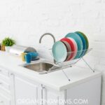 White kitchen with colorful dishes drying by clean sink.