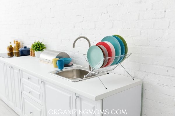 White kitchen with colorful dishes drying by clean sink.