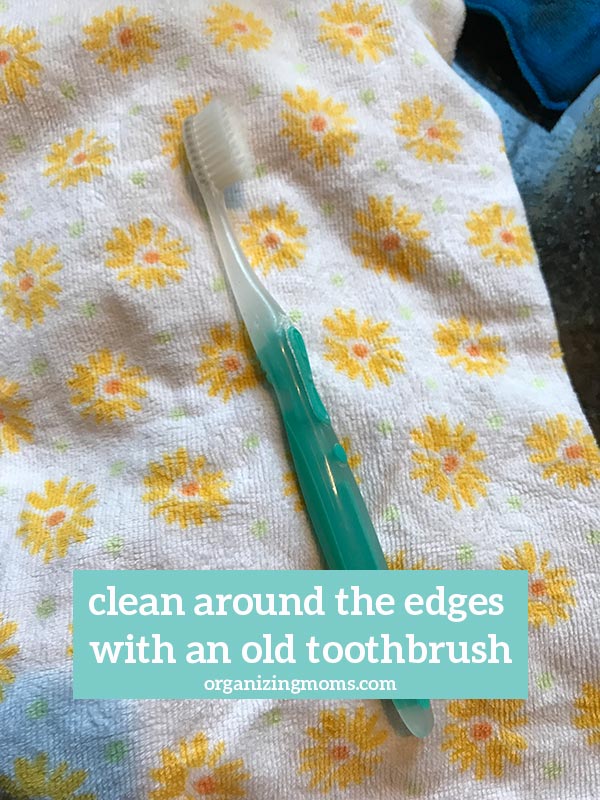 Text - clean around the edges with an old toothbrush organizingmoms.com. Image of a teal toothbrush on a towel with flower pattern