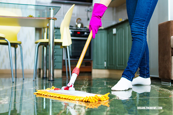 Close up of person cleaning a floor with a yellow dust mop