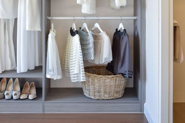 A closet with hanging clothes and a closet basket on the floor.