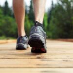 woman wearing dark sneakers walking across wood bridge to symbolize meeting daily step goal