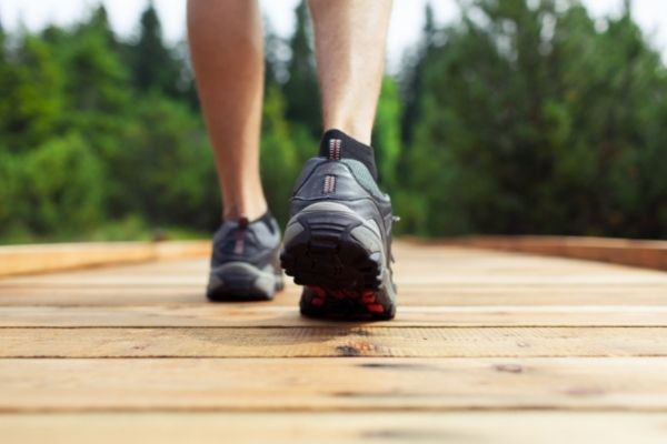 woman wearing dark sneakers walking across wood bridge to symbolize meeting daily step goal