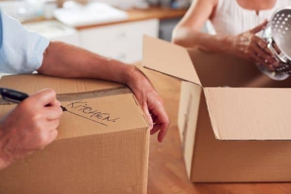 two boxes being filled with kitchen items to symbolize decluttering and downsizing