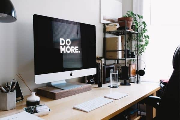 desk with monitor that says do more and white keyboard plant in background