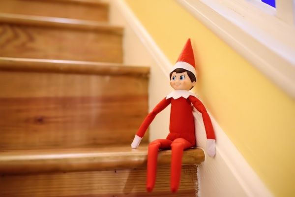 elf on the shelf sitting on wooden stairs with white and yellow wall in background