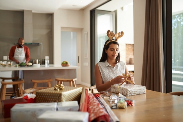 girl wrapping presents at table while her father cooks in kitchen