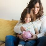 mom and daughter saving money in piggy bank sitting on sofa