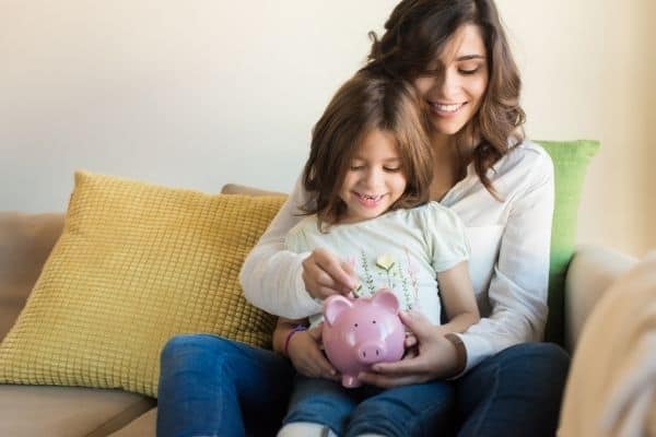 mom and daughter saving money in piggy bank sitting on sofa