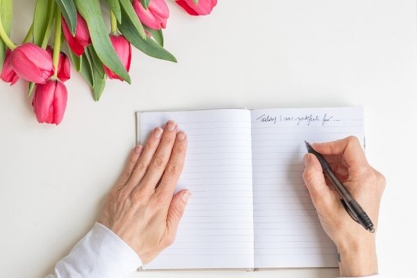 A close up of a person writing a grateful list, a flower