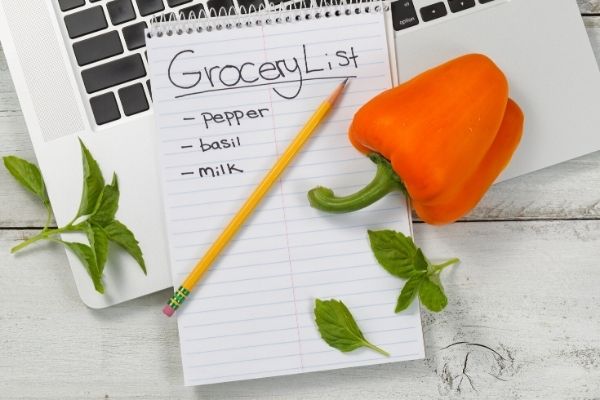 Grocery list on top of keyboard with red pepper and herbs surrounding