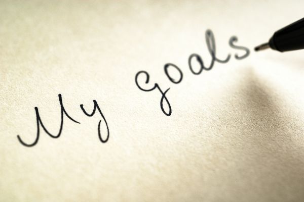 black pen writing out "my goals" on paper to symbolize handwritten goals