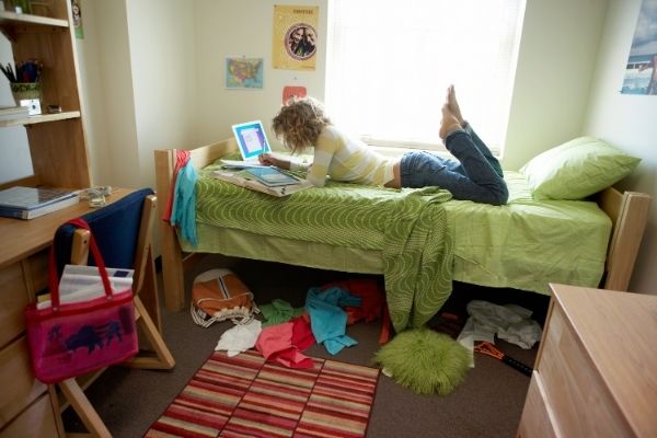 girl on bed in cluttered dorm room