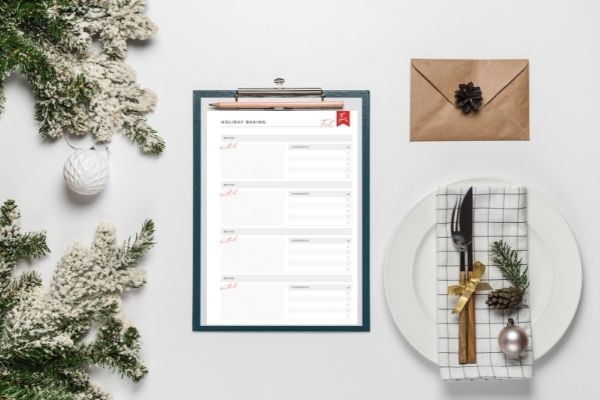 Printable holiday baking on a clipboard surrounded by evergreen branches and place settings and invitations