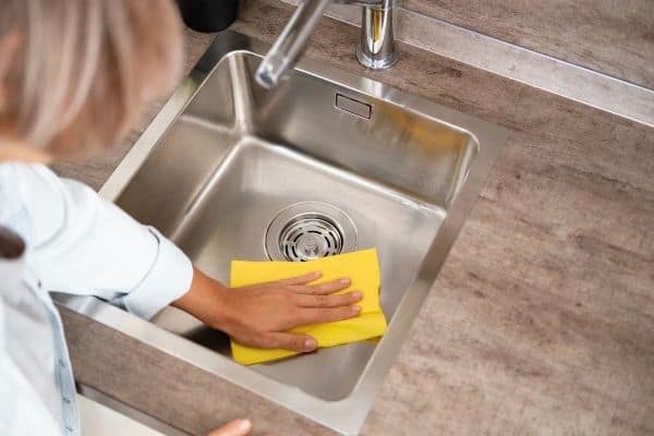 woman wiping sink with yellow cloth to symbolize household habits