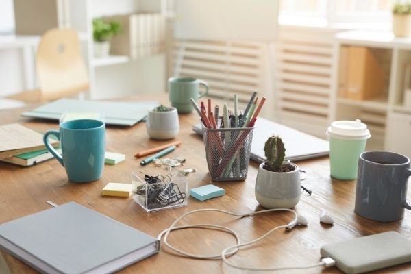 cluttered desk with post its, cords, plants, mugs