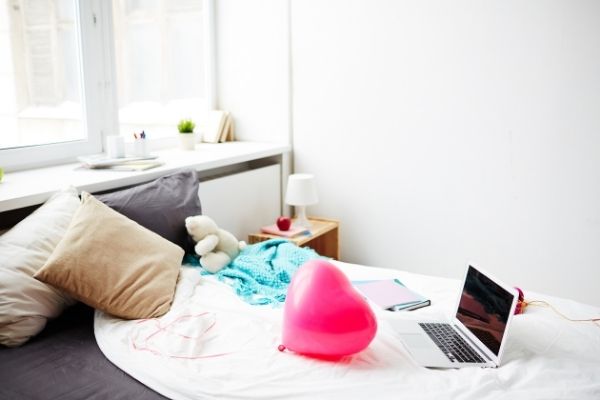 Unmade bed with computer, balloon. For how to start decluttering your room article.