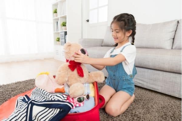 girl packing teddy bear in suitcase for trip