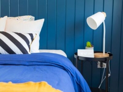 made bed with blue covers, striped pillow, blue wall, nightstand