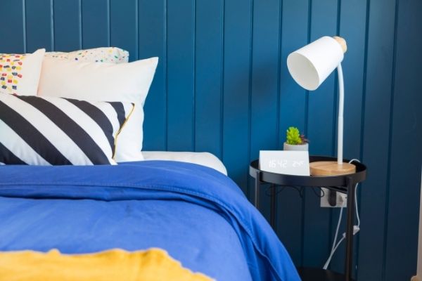 made bed with blue covers, striped pillow, blue wall, nightstand