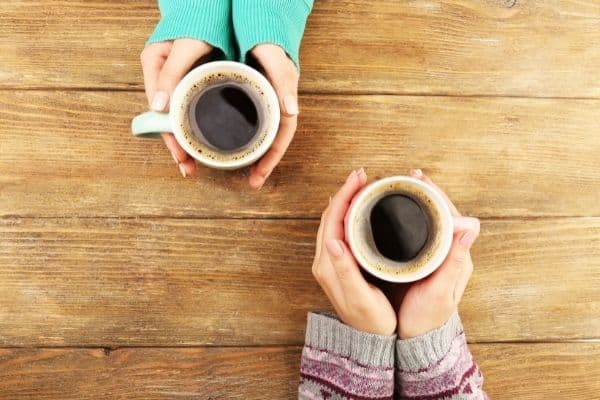 two people holding coffee cups on wooden table