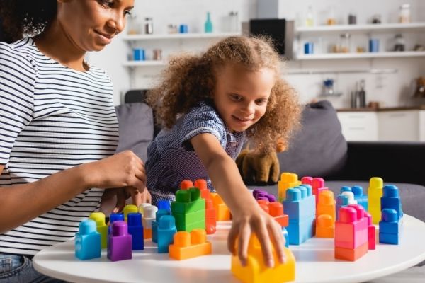 mothers helper and girl playing with duplos