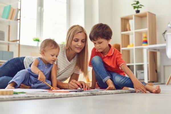 mother's helper playing with two kids on the floor