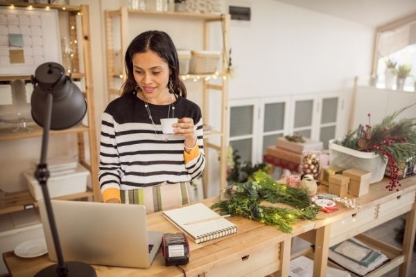 woman ordering christmas supplies online while sipping coffee and surrounded by christmas decor