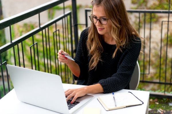 A woman sitting at a table with a laptop and smiling at her credit card while ordering online