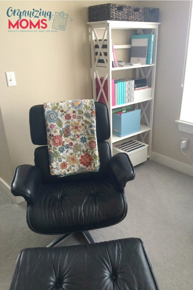 Black chair with floral blanket. Organized bookshelf in background.