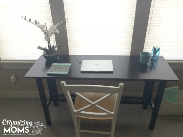 Desk with laptop, plant, jar of pens, coffee, in front of window.