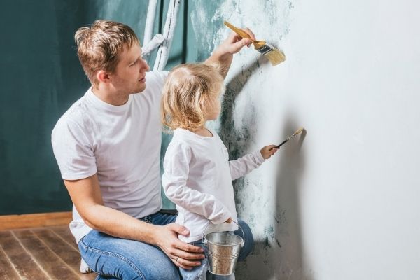 Dad and young child painting a wall white